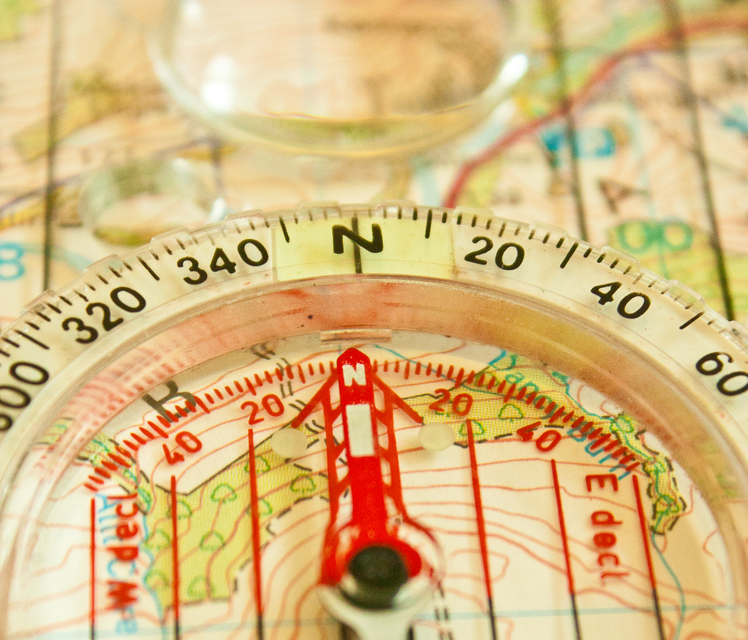 A close up of a compass needle pointing North, with the background being an OS map.