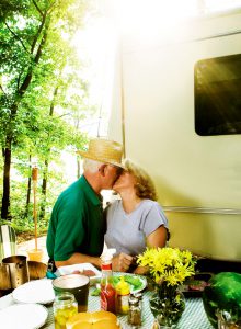 A senior couple kissing while sitting in front of their RV at the picnic table.